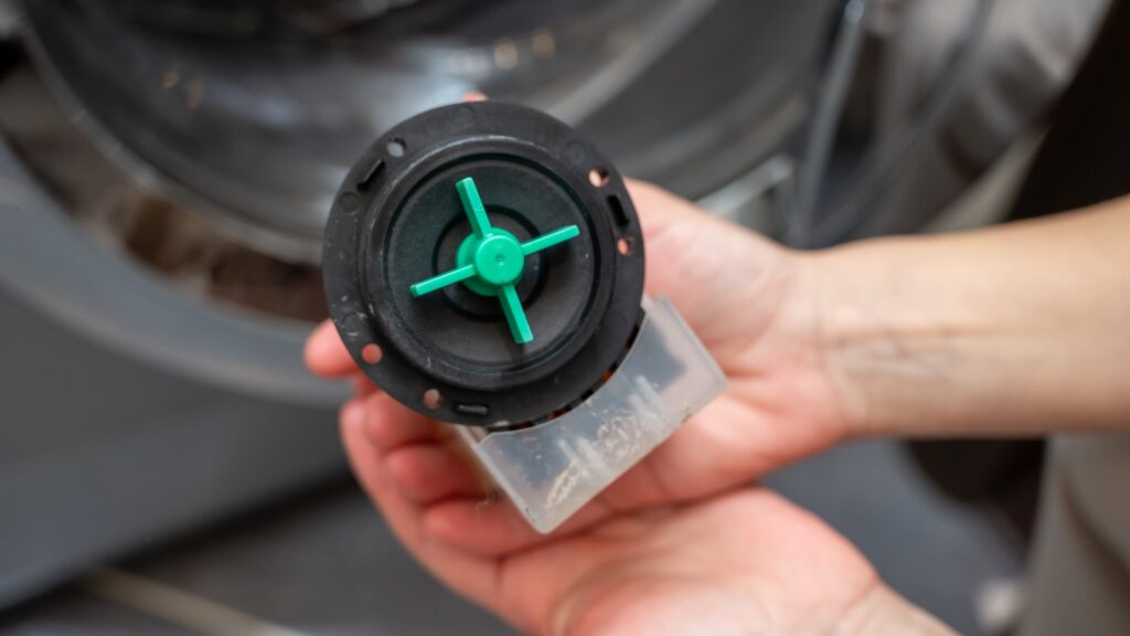 Two hands holding the drain pump filter just removed from a front load washing machine