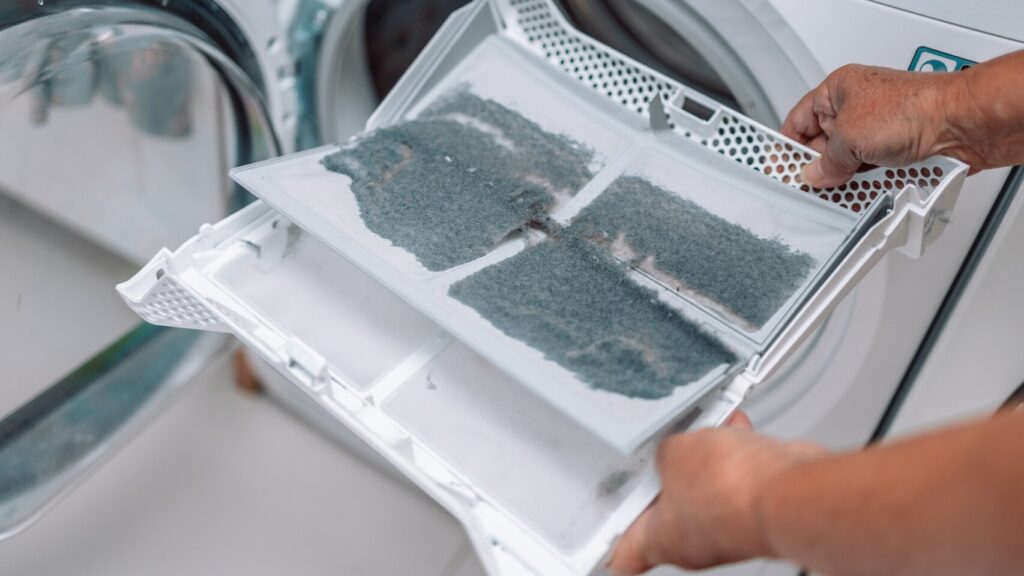 A hand wiping the metal moisture sensor strips inside a clothes dryer drum with a cloth