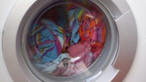 Colorful laundry spinning inside the drum of a front load washing machine behind the door glass