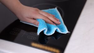A hand wiping a black glass cooktop with a blue microfiber cloth