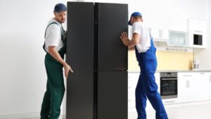 Two workers carrying a large new refrigerator into a modern kitchen