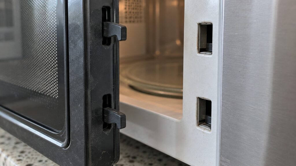 A close view of a microwave door latch and the recesses it engages in the frame