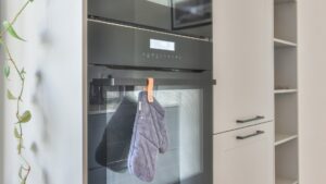 Built-in ovens stacked in a tall white kitchen cabinet beside open shelving